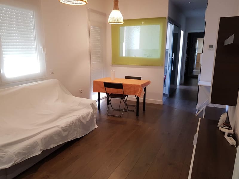 Salón de un piso en alquiler antes de la puesta a punto de Inmperson: sofá tapado con una sábana y muebles sin ordenar